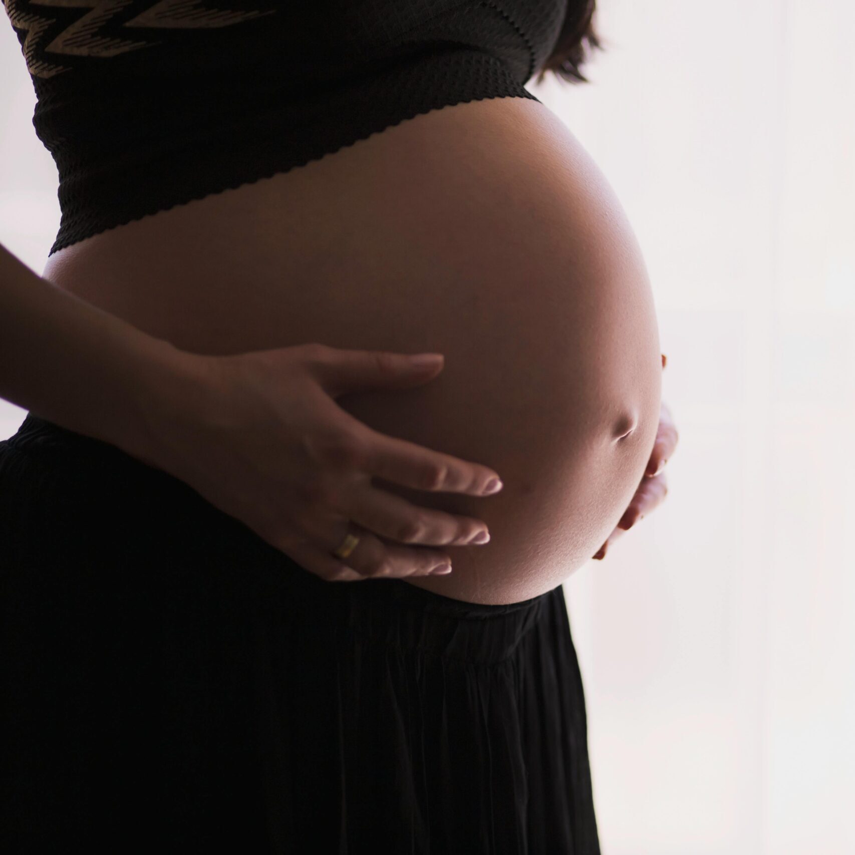 A close-up of a pregnant woman touching her bare belly, expressing warmth and care.
